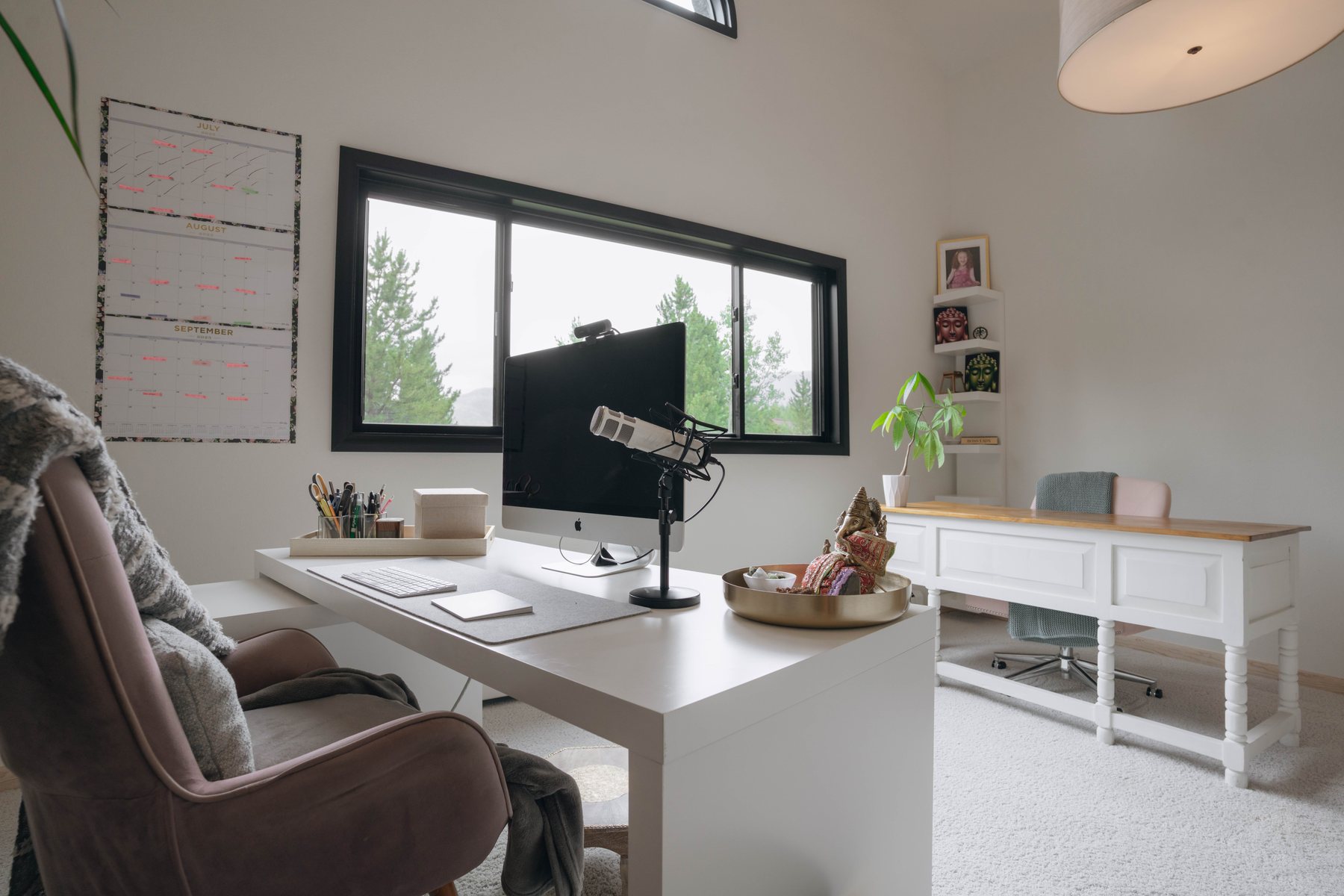 The office: two full desks side by side under a wide forest-view window